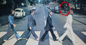 Four men crossing a zebra crossing on a street, with one of them circled in red. cars are parked on both sides of the road, under a clear sky.