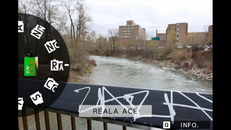 Image showing a concrete balcony with graffiti over a river; in focus on the left is a blurred cylindrical green object. A cityscape with buildings appears in the background.