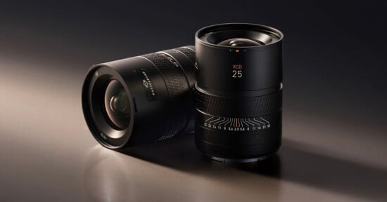 Two Hasselblad 25mm f/2.5V lenses placed on a reflective surface with lighting highlighting their details and markings, one facing up and the other on its side.