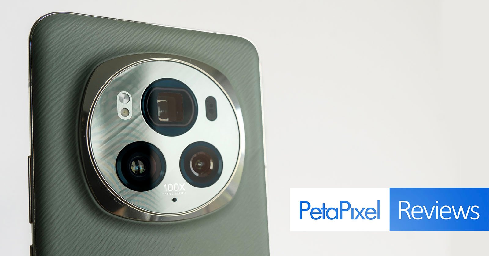 Close-up of a smartphone's camera setup featuring multiple lenses and "100x" label, against a light grey background, with a "petapixel reviews" logo in the corner.