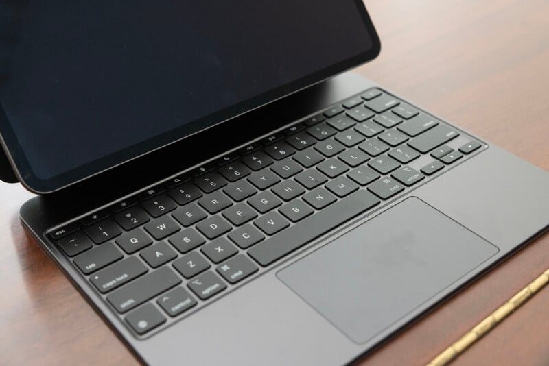 A modern laptop on a wooden desk, showing a partial view of the black keyboard and trackpad, with the screen tilted slightly down.