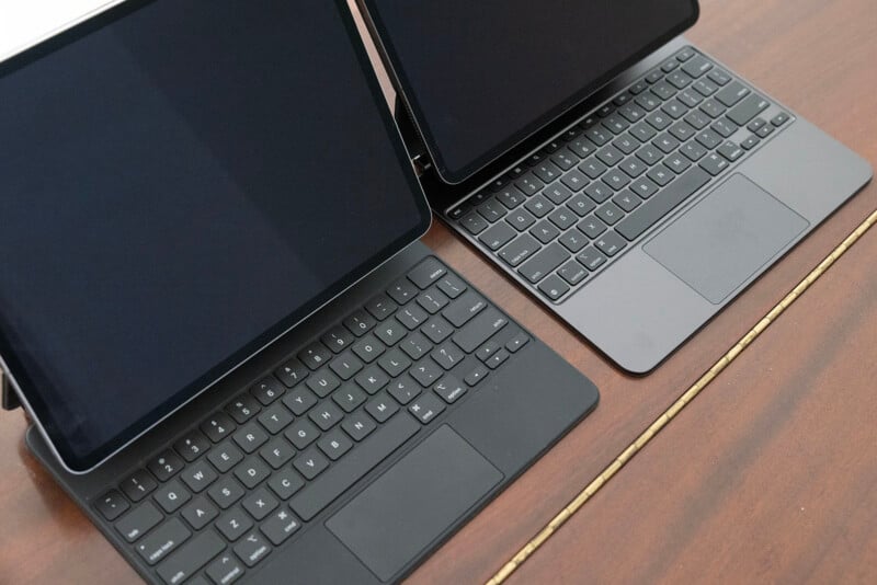 Two laptops with black keyboards are positioned side by side on a wooden desk, both screens are turned off and folded at an angle.