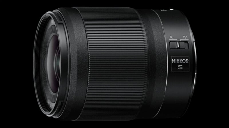 A black NIKKOR S camera lens with textured grip and visible controls for manual (M) and automatic (A) focus adjustments. The lens is placed against a solid black background, highlighting its detailed design and features.