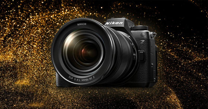 A Nikon camera with a large lens is displayed against a glittering gold background. The camera has a prominent Nikon logo and a Z series mark, indicating it is part of Nikon's Z series lineup. The lens reads "NIKKOR 24-70mm.