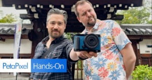 Two men are standing in front of a traditional Japanese building. One man holds a blue camera towards the viewer. The PetaPixel logo and the text "Hands-On" are displayed in the bottom left corner.