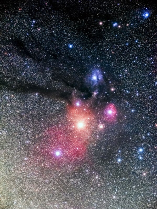 A vibrant and detailed telescopic image of a star-filled region in space. The stars vary in color, from blue and white to vivid red and pink. Nebulous clouds are visible, contributing to the colorful celestial display set against the black background of space.