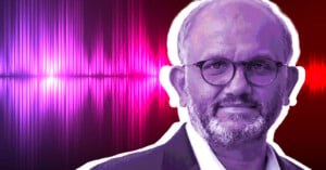 Shantanu Narayan with glasses and a beard, wearing a suit jacket, is shown against a vibrant background of pink and red soundwaves. The image has a purple tint and a white outline around the person, giving a graphic design effect.