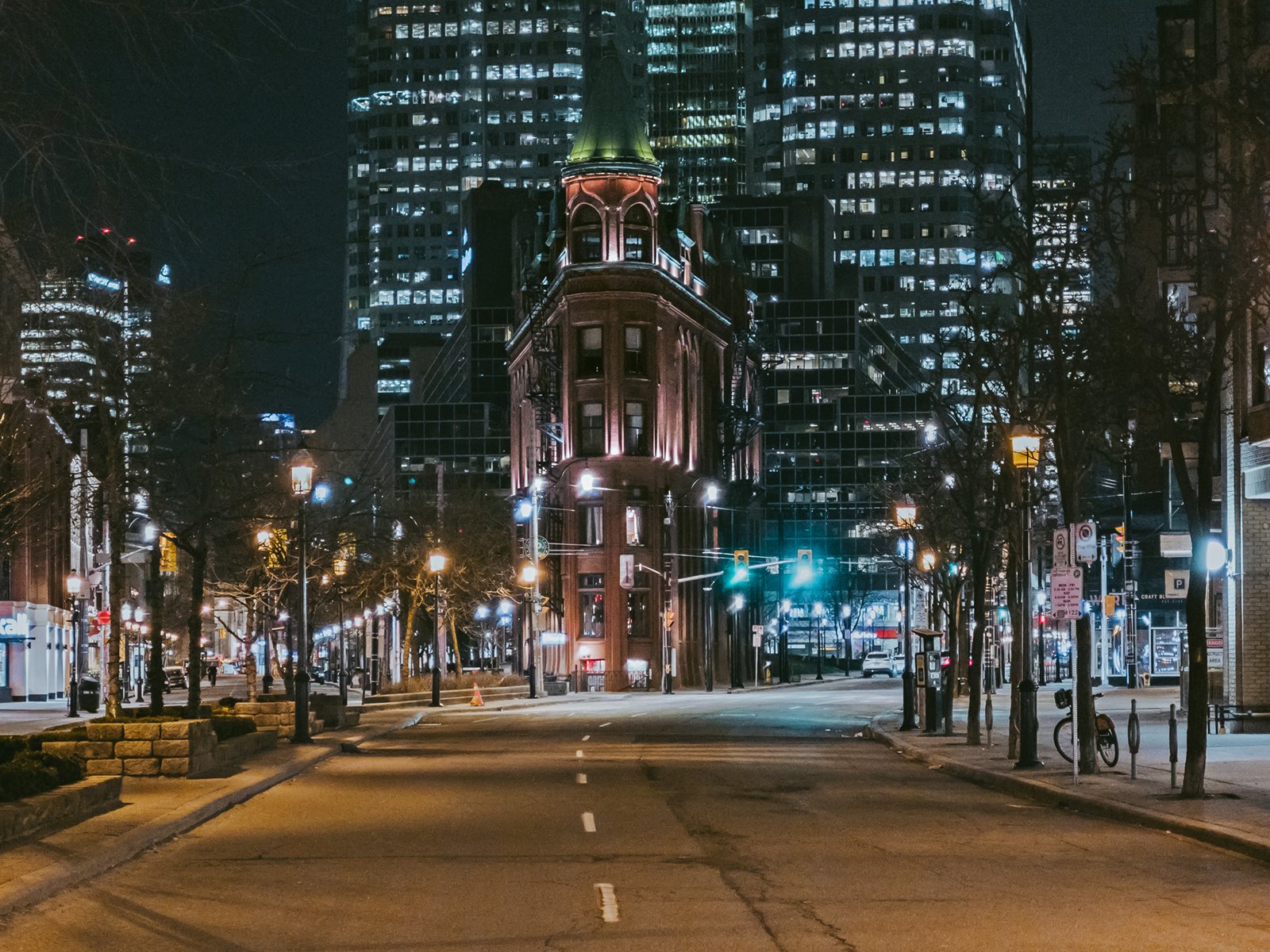 Night view of a city street with a vintage, illuminated turret-style building at the center, flanked by modern high-rises. empty streets and traffic lights emphasize the quiet, urban setting.